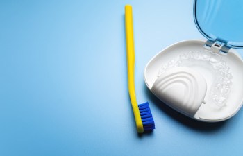 Clear aligner in a case next to a yellow and blue toothbrush