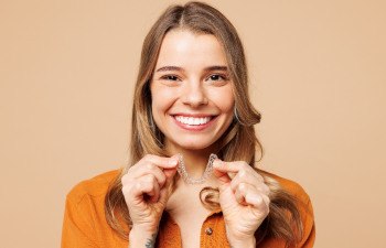 Girl with brown hair in orange shirt smiling holding Invisalign