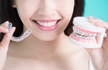 Nose-to-chest closeup of someone holding up model teeth with braces and Invisalign to compare