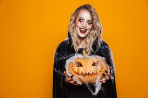 Woman in witch costume smiling and holding a pumpkin on orange background