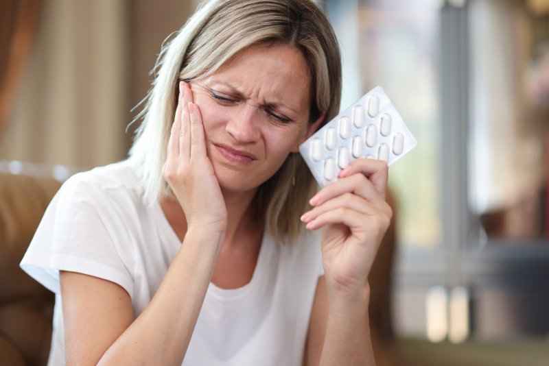 A young woman suffering from tooth pain and holding a blister of pills